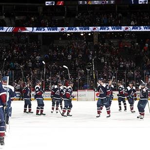 An image of a hockey team on ice raising there sticks celebrating.