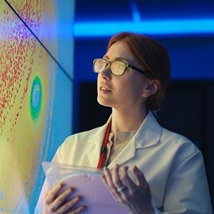 woman in white lab coat holding a silicon wafer in front of a colorful wall