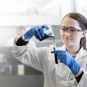 woman in white lab coat pouring liquid from beaker into test tube